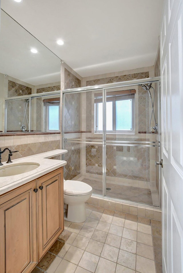 bathroom featuring tile patterned flooring, tile walls, a shower with shower door, toilet, and vanity