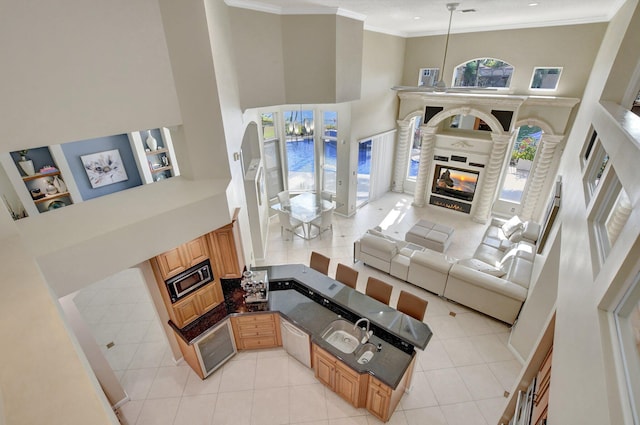 living room featuring a towering ceiling, sink, ornamental molding, and light tile patterned floors