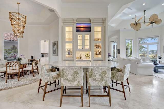 bar with a high ceiling, hanging light fixtures, ornamental molding, and ceiling fan with notable chandelier