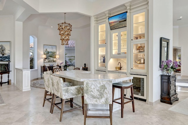 dining space featuring a towering ceiling, an inviting chandelier, wine cooler, and crown molding