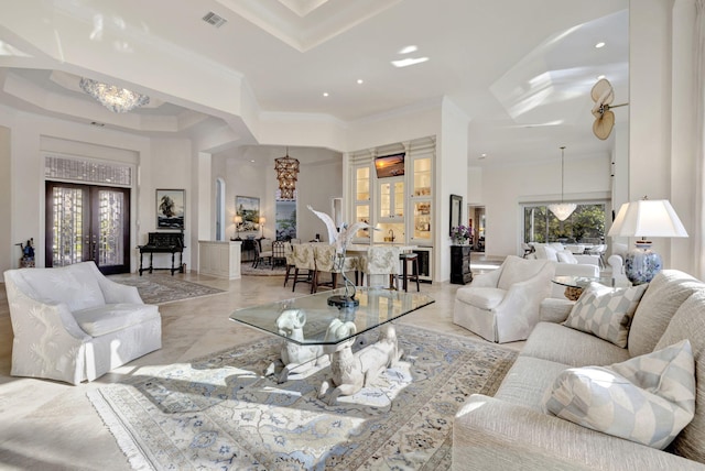 living room with ceiling fan with notable chandelier, a high ceiling, a raised ceiling, and crown molding