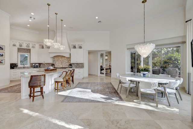 kitchen with custom exhaust hood, a large island with sink, pendant lighting, white cabinets, and backsplash