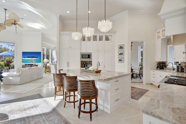 kitchen with light stone countertops, pendant lighting, stainless steel appliances, a center island with sink, and white cabinets