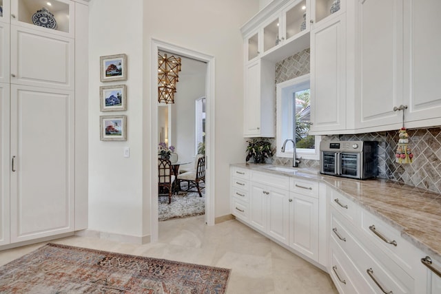 kitchen with sink, white cabinetry, tasteful backsplash, and light stone counters