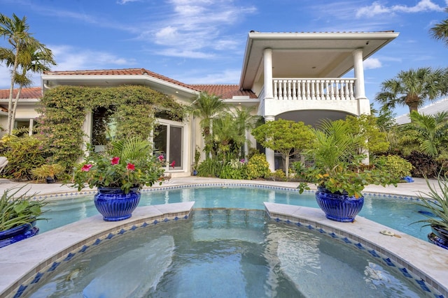 back of property featuring a balcony and an in ground hot tub