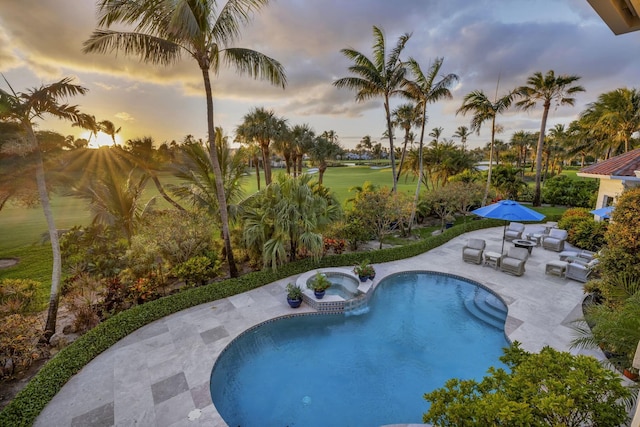 pool at dusk with a patio and an in ground hot tub