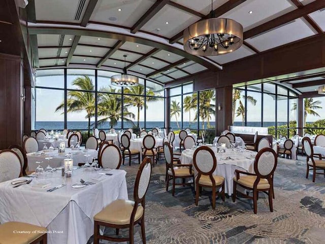 carpeted dining room featuring coffered ceiling, an inviting chandelier, and a water view