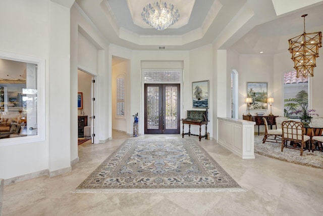 entrance foyer with crown molding, a notable chandelier, french doors, a tray ceiling, and a high ceiling