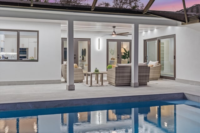 pool at dusk with an outdoor living space, ceiling fan, glass enclosure, and french doors