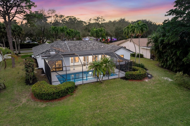 back house at dusk featuring a lawn, a patio area, and a lanai