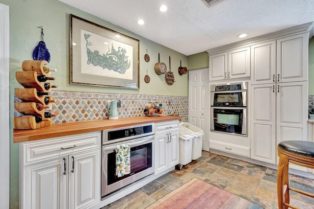 kitchen featuring wooden counters, a textured ceiling, white cabinetry, and double oven