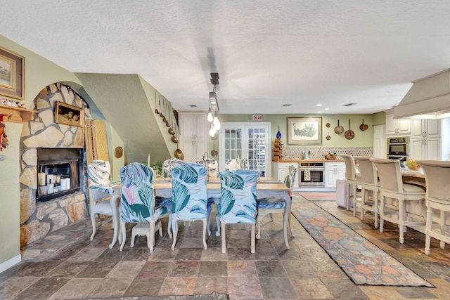 dining room with a stone fireplace, french doors, and a textured ceiling