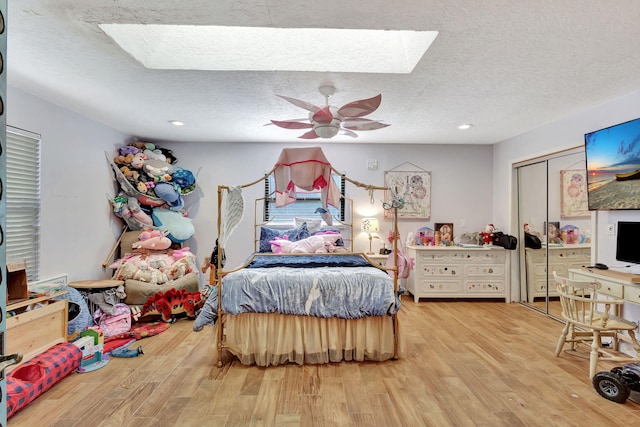 bedroom with hardwood / wood-style floors, a textured ceiling, a skylight, and ceiling fan