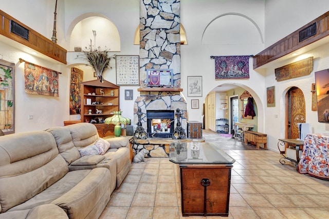 living room with a stone fireplace, a towering ceiling, and light tile patterned floors