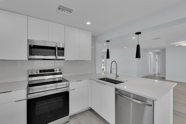 kitchen featuring white cabinets, sink, decorative light fixtures, kitchen peninsula, and stainless steel appliances