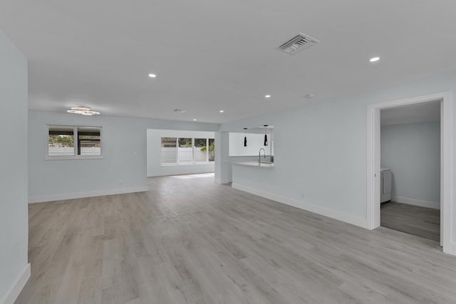 unfurnished living room featuring sink, a healthy amount of sunlight, and light hardwood / wood-style flooring