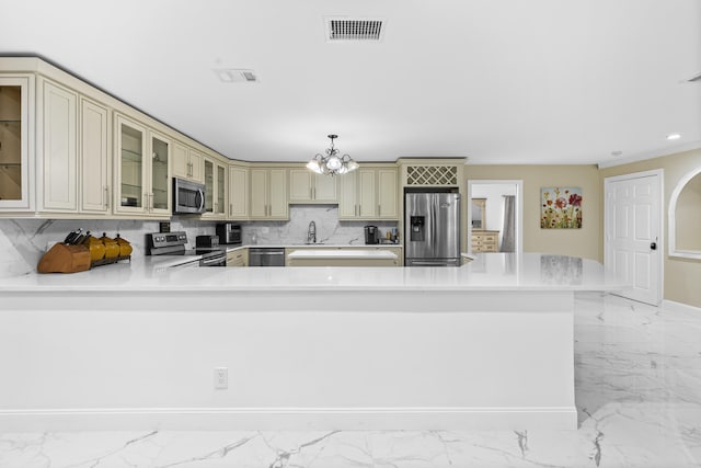 kitchen with appliances with stainless steel finishes, tasteful backsplash, a chandelier, hanging light fixtures, and cream cabinets