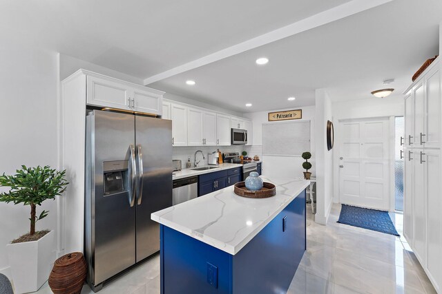 kitchen with white cabinetry, appliances with stainless steel finishes, light stone countertops, a kitchen island, and sink