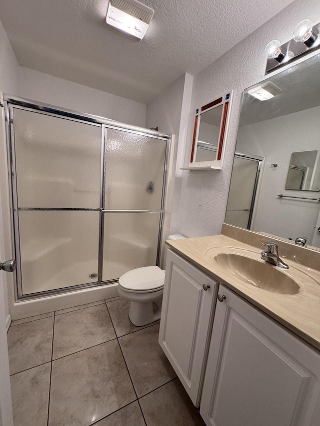 bathroom with toilet, a textured ceiling, walk in shower, tile patterned flooring, and vanity