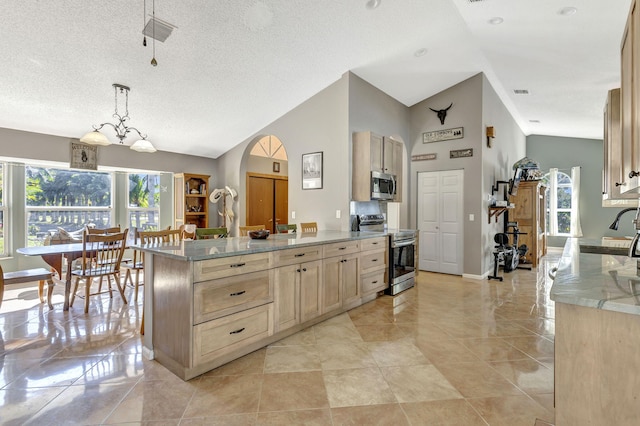 kitchen with light brown cabinetry, hanging light fixtures, lofted ceiling, and appliances with stainless steel finishes