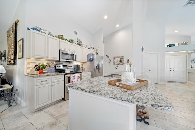 kitchen with sink, stainless steel appliances, light stone counters, backsplash, and white cabinets