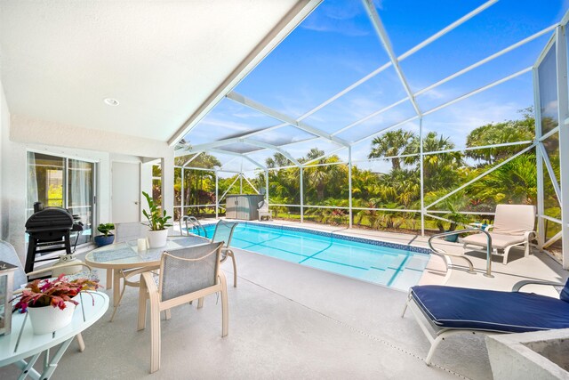 view of pool with glass enclosure, a grill, and a patio