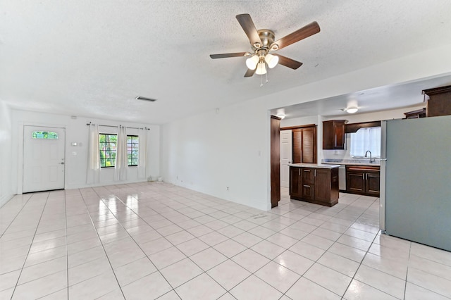 unfurnished living room with ceiling fan, light tile patterned flooring, sink, and a textured ceiling