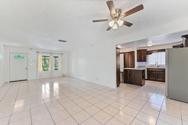 unfurnished living room with a textured ceiling, ceiling fan, light tile patterned floors, and sink