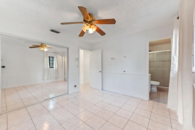 unfurnished bedroom featuring ensuite bath, ceiling fan, a textured ceiling, a closet, and light tile patterned flooring