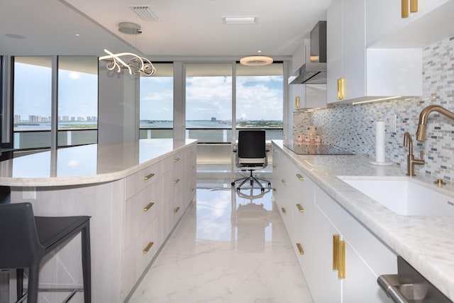 kitchen featuring a water view, wall chimney range hood, white cabinets, and decorative light fixtures