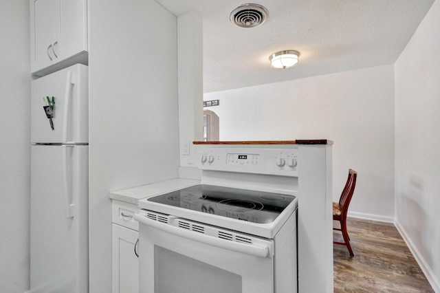 kitchen with white cabinetry, light wood-type flooring, a textured ceiling, and white appliances