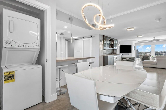 dining space featuring a barn door, ceiling fan, crown molding, and stacked washing maching and dryer