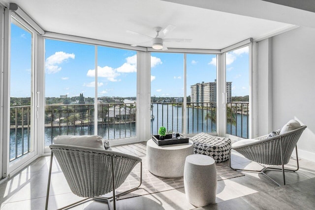 sunroom with ceiling fan and a water view