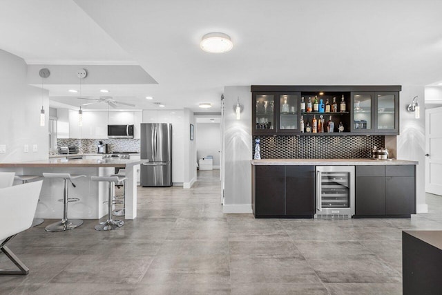 bar with tasteful backsplash, ceiling fan, beverage cooler, and appliances with stainless steel finishes