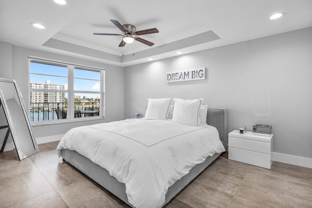 bedroom with a raised ceiling, ceiling fan, and a water view