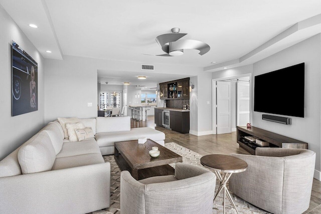 living room featuring hardwood / wood-style floors, ceiling fan, wine cooler, and bar area