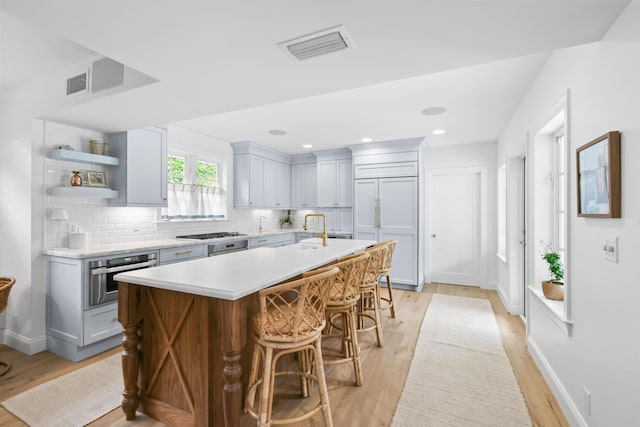 kitchen featuring light hardwood / wood-style flooring, a breakfast bar, stainless steel appliances, tasteful backsplash, and a center island with sink