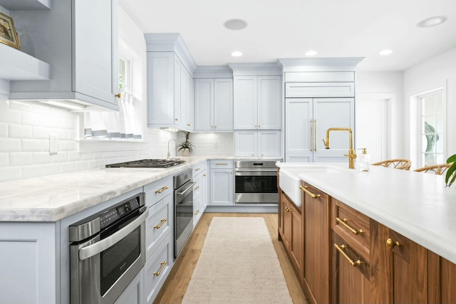 kitchen with sink, light stone counters, light hardwood / wood-style flooring, appliances with stainless steel finishes, and decorative backsplash