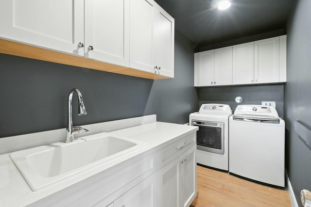 clothes washing area with cabinets, sink, independent washer and dryer, and light hardwood / wood-style flooring