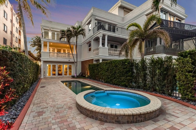 back house at dusk with a swimming pool with hot tub