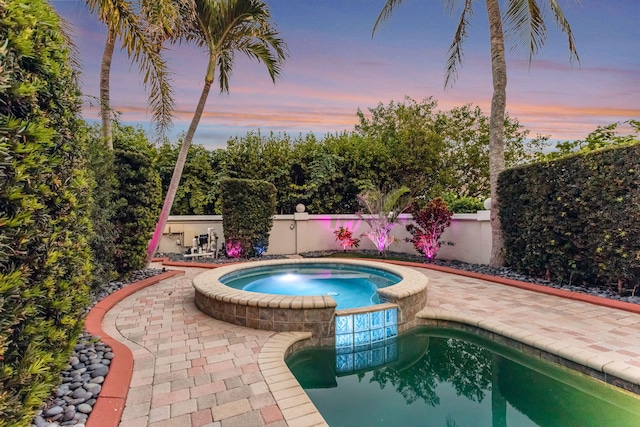 pool at dusk with an in ground hot tub and a patio