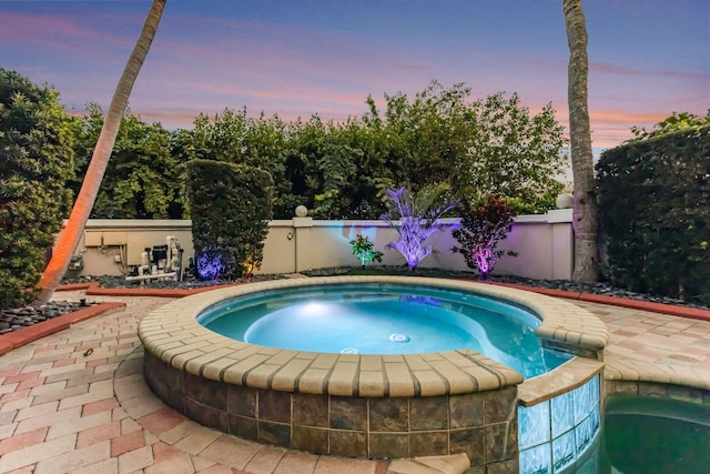 pool at dusk featuring an in ground hot tub and a patio area