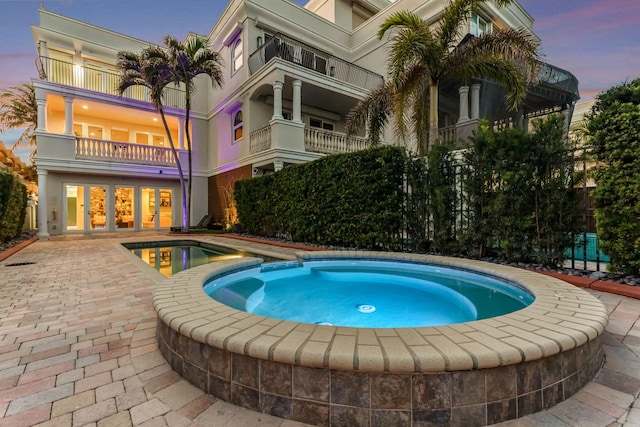 pool at dusk featuring an in ground hot tub and a patio area