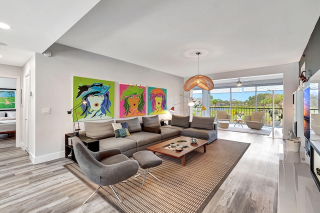 living area featuring baseboards, light wood-style floors, and a ceiling fan