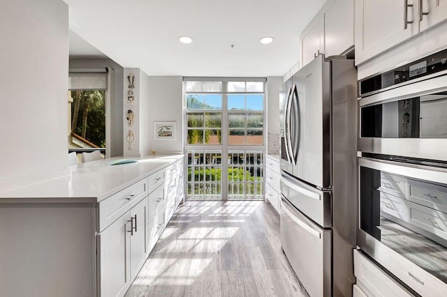 kitchen with white cabinets, expansive windows, stainless steel appliances, and light hardwood / wood-style flooring