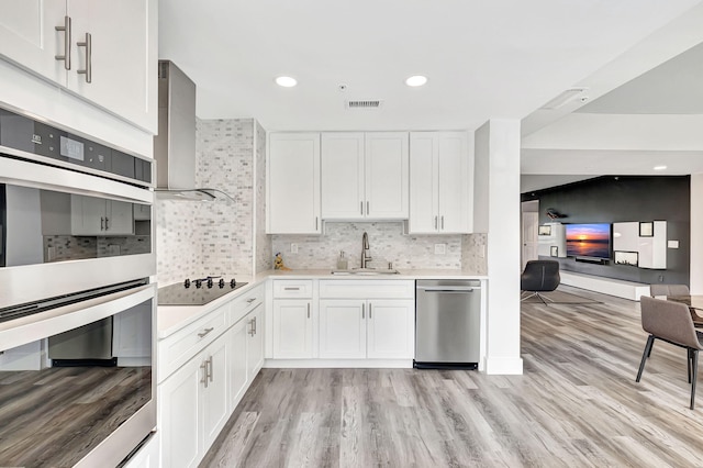 kitchen featuring visible vents, wall chimney range hood, light countertops, stainless steel appliances, and a sink