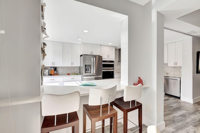 kitchen with backsplash, a breakfast bar area, white cabinetry, kitchen peninsula, and stainless steel appliances