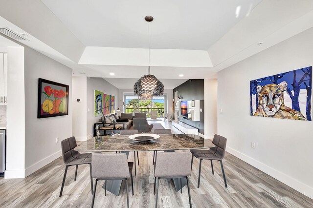 dining space with light wood-type flooring and a tray ceiling