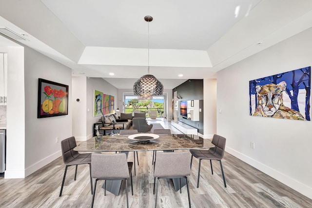 dining space with baseboards, a raised ceiling, and light wood-style flooring