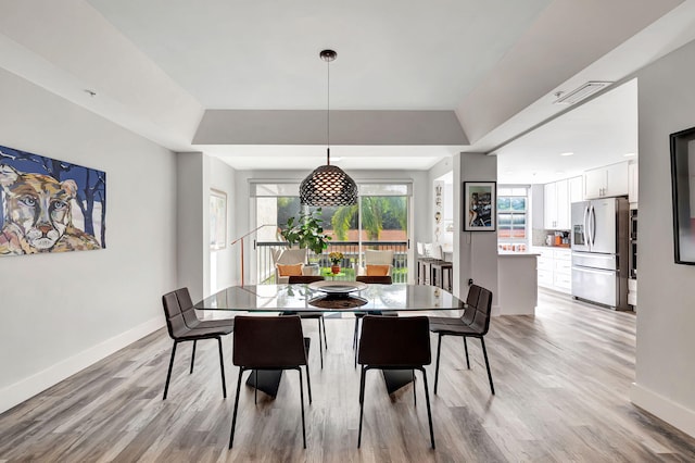 dining space featuring baseboards, light wood-type flooring, and a tray ceiling